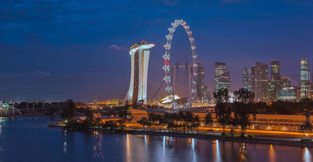 Stunning night view of Singapore with Marina Bay Sands and Ferris Wheel, reflecting city lights on water.